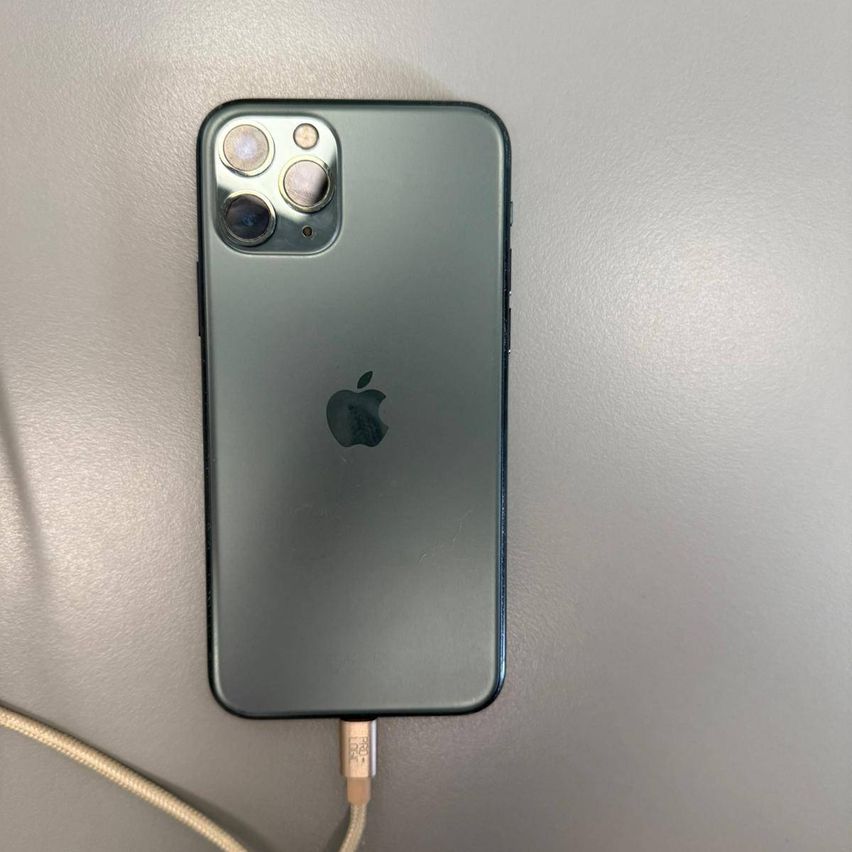 Die Rückseite eines Apple iPhones, möglicherweise ein iPhone 11 Pro, das an ein Ladekabel angeschlossen ist und auf einer grauen Oberfläche ruht.