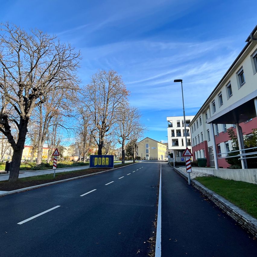 Eine leere Straße mit einem blauen Schild, das DORA sagt. Auf der rechten Seite der Straße befinden sich Gebäude.