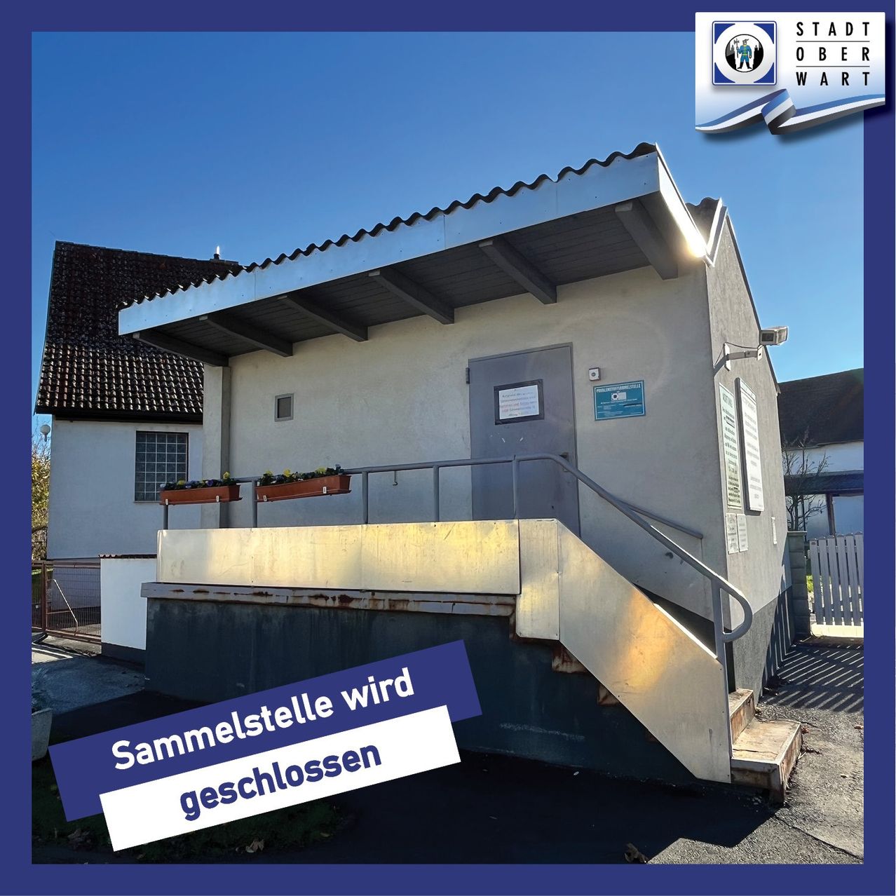 Das Bild zeigt ein kleines Gebäude mit einem geneigten Dach und einer Treppe. Es hat eine graue Tür und ein blaues Schild mit den Worten 'Sammelstelle wird geschlossen'. Dahinter befindet sich ein weißer Zaun und ein Haus.