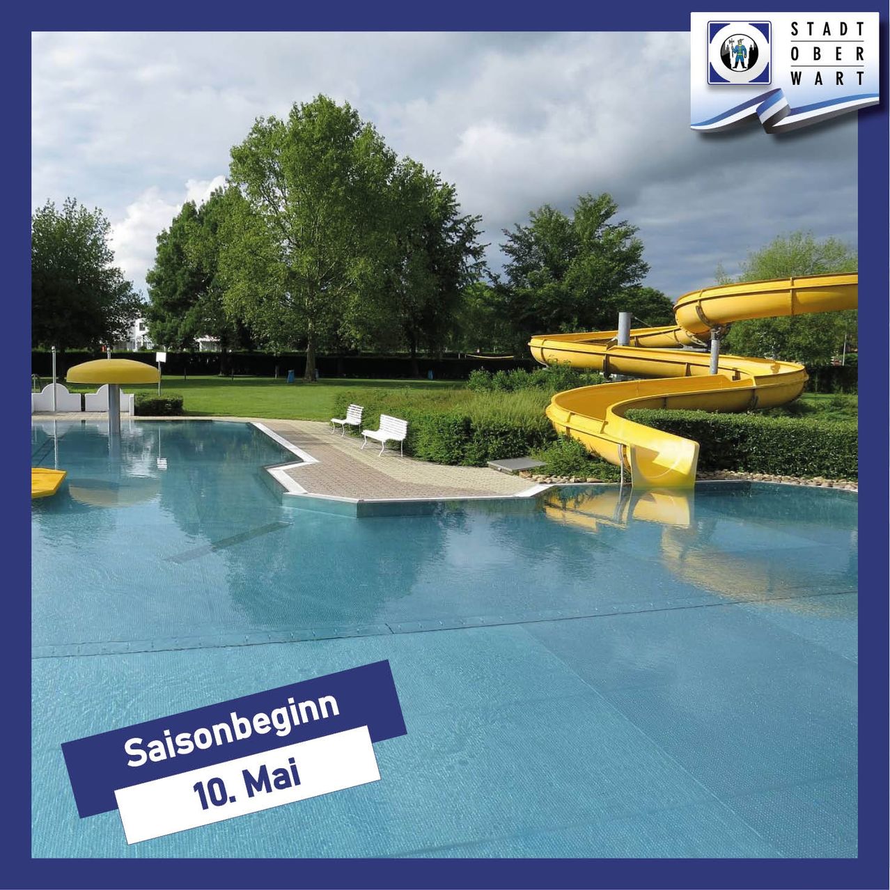 Freibad mit einer gelben Wasserrutsche. Die Saison beginnt am 10. Mai. Bäume und Pflanzen sind im Hintergrund.