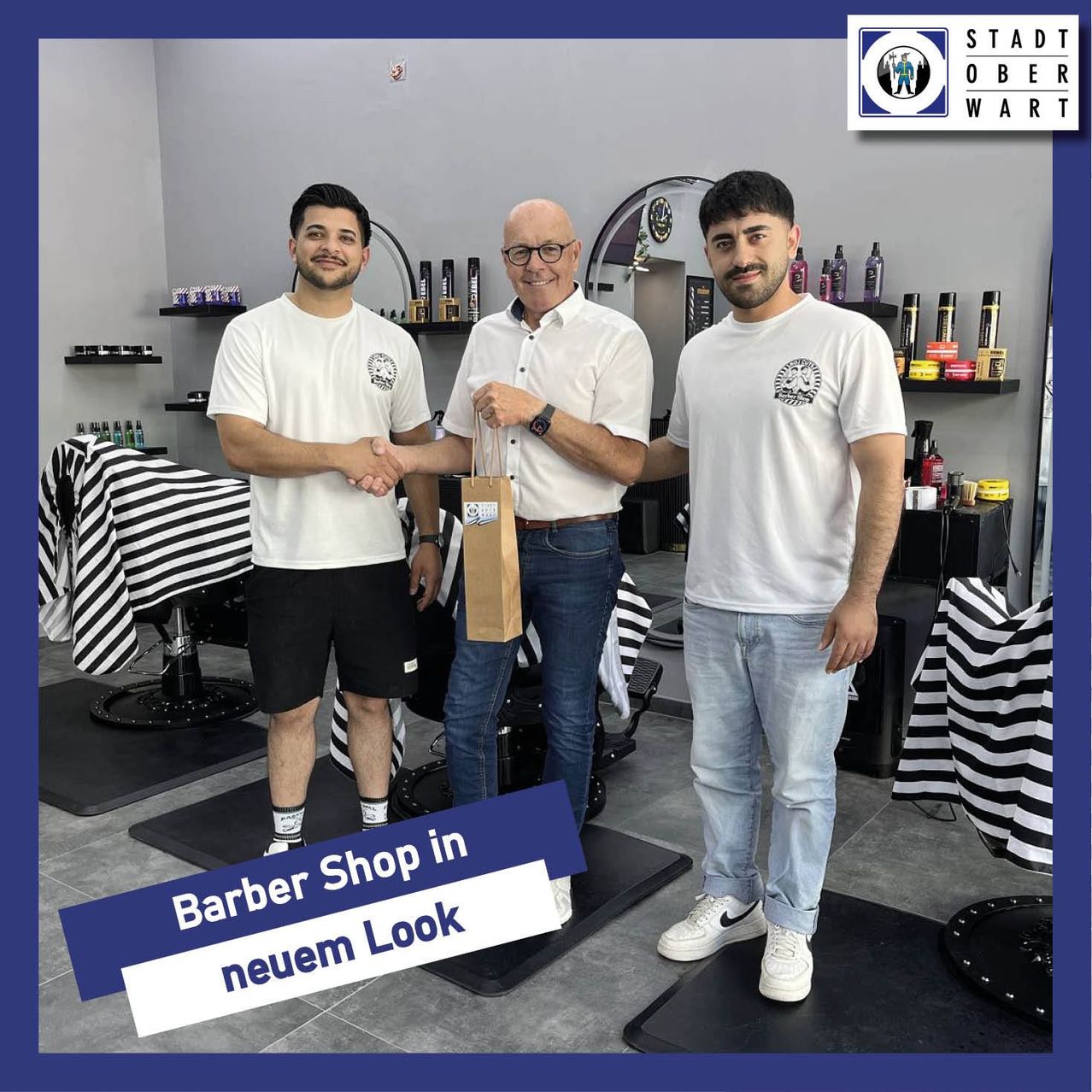 Drei Männer in einem Barbershop, zwei von ihnen schütteln Hände, und der Mann in der Mitte hält einen braunen Beutel. Sie tragen alle weiße T-Shirts und Jeans. Hinter ihnen steht ein Schreibtisch mit einer schwarzen Matte.
