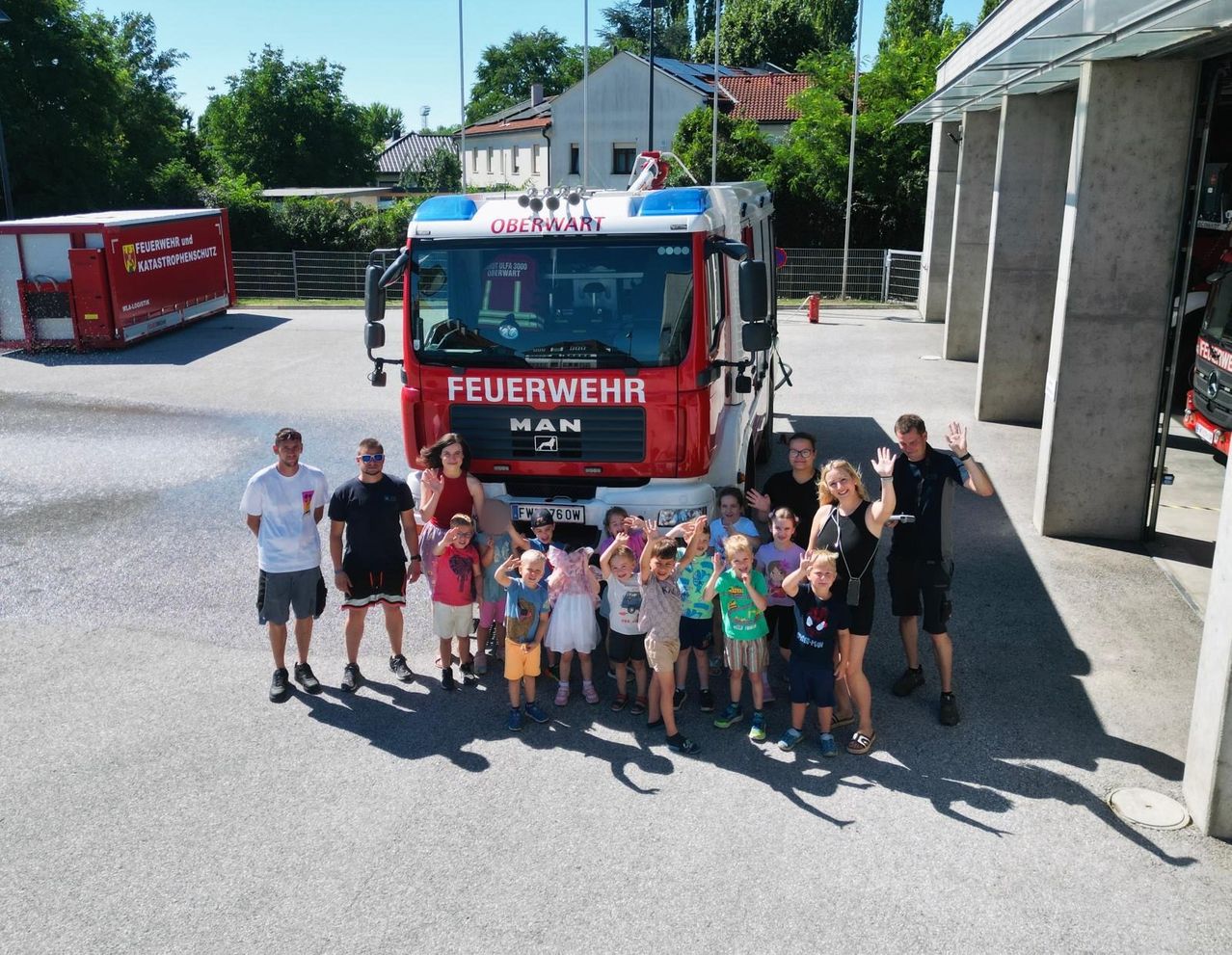 Eine Gruppe von Erwachsenen und Kindern steht vor einem roten Feuerwehrauto. Sie alle lächeln und posieren für ein Foto. Das Feuerwehrauto hat den Schriftzug Oberwart an seiner Seite.
