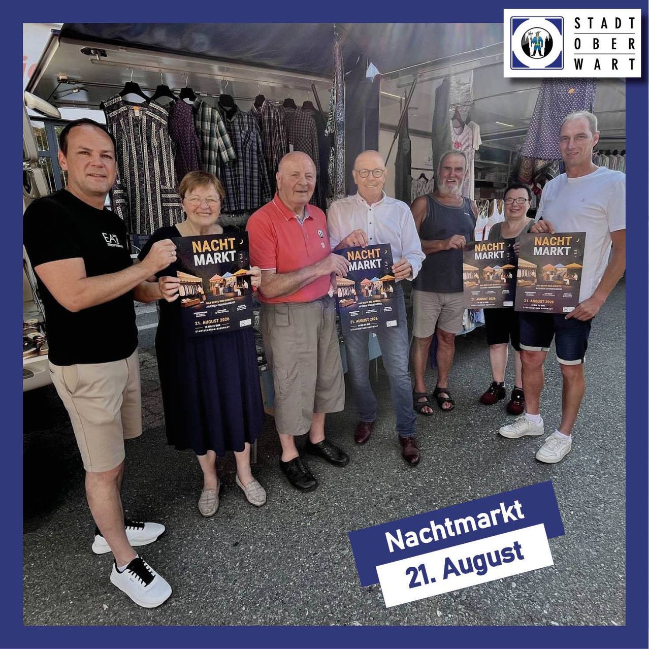 A group of people holding banners stand in front of a clothing store. They are smiling and posing for a picture.