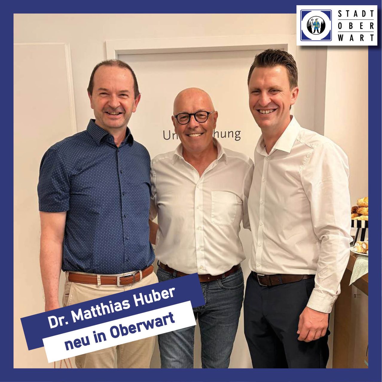 Three men stand together smiling for a photo, one is wearing a blue shirt and khaki pants, another is wearing a white shirt and glasses, and the third is in a white shirt and black pants.