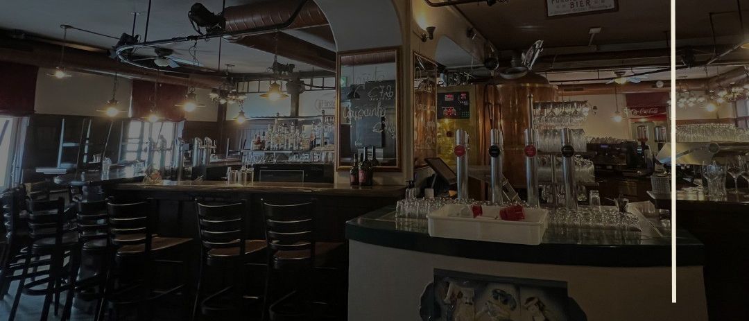 Das Innere einer Brauerei mit Theke, Regalen und einer Speisekarte. Der Raum ist gut beleuchtet mit verschiedenen Lampen und Kronleuchtern.
