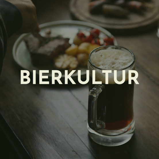 Ein Nahaufnahme eines Glaskrugs mit dunklem Bier auf einem Holztisch mit dem Wort Bierkultur in weißen Buchstaben. Eine Hand schneidet Fleisch auf einem Teller mit Gemüse.