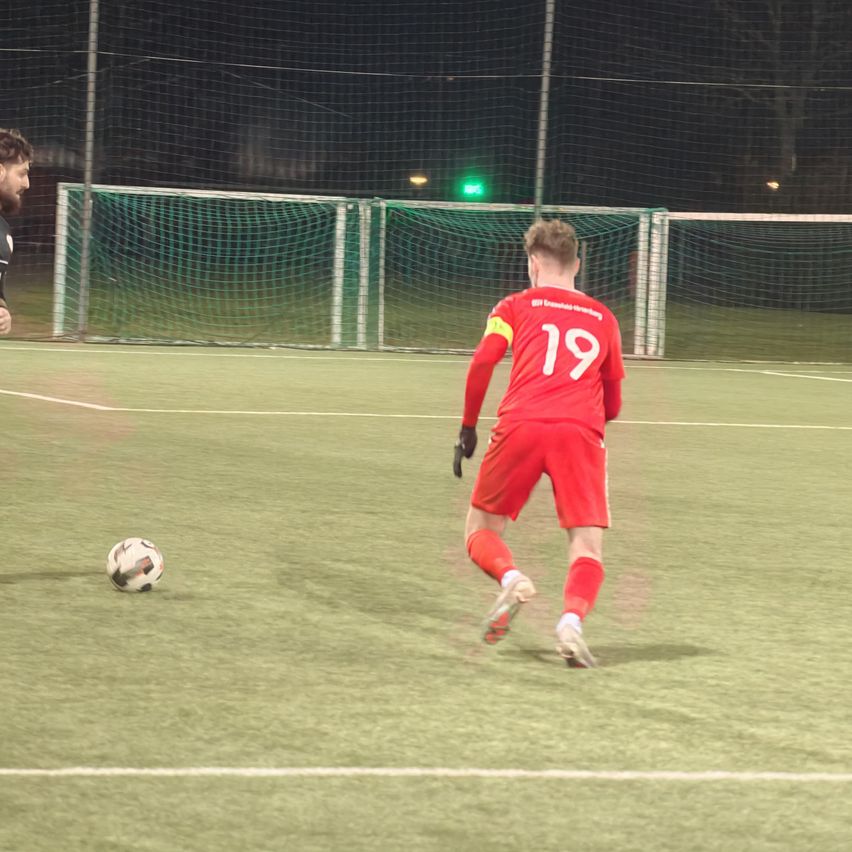 Ein Fußballspieler in einem roten Trikot mit der Nummer 19 läuft nachts auf einem Feld auf den Ball zu.