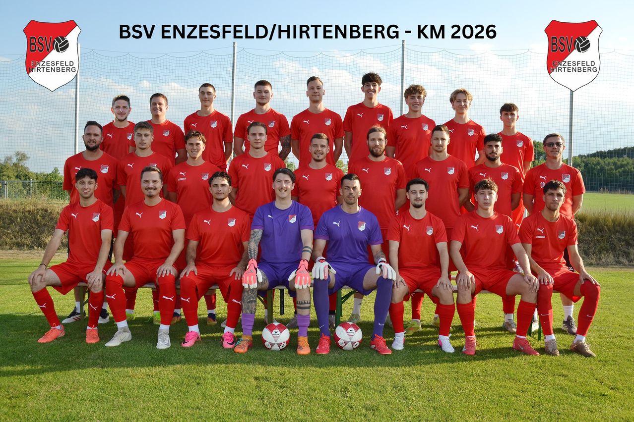 A soccer team in red jerseys poses for a team photo with two players in purple jerseys sitting in the middle.