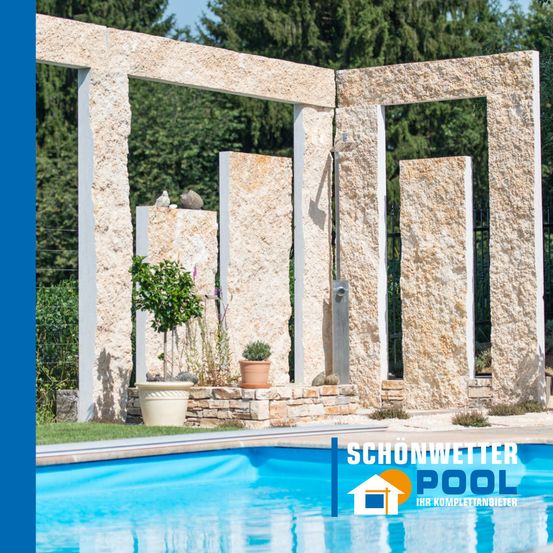 Ein Freibad mit einer Steinstruktur und einer Dusche, umgeben von Grün und einem blauen Himmel mit Bäumen im Hintergrund.
