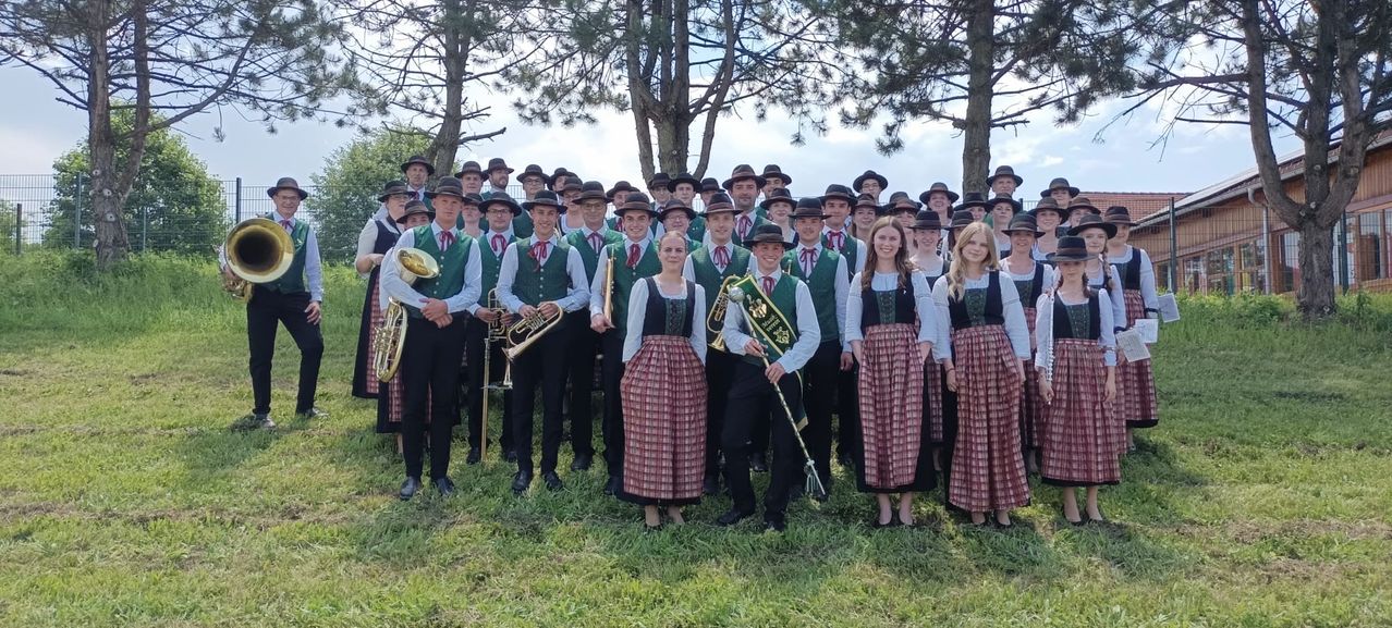 Eine Gruppe von Menschen in traditioneller Kleidung, möglicherweise eine Band, posiert für ein Foto auf einer Rasenfläche mit Bäumen im Hintergrund.