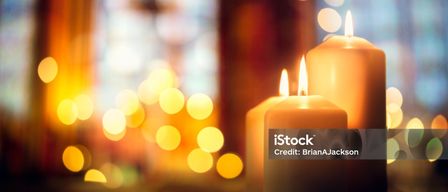 Drei Kerzen sind auf einem Holztisch entzündet, mit warmem gelbem Licht. Der Hintergrund ist verschwommen mit hellen gelben Lichtern. iStock-Wasserzeichen ist sichtbar.