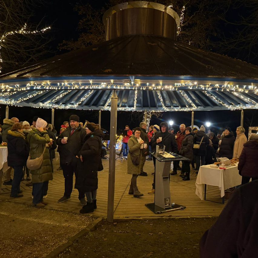 Eine nächtliche Zusammenkunft unter einem Pavillon mit Menschen, die plaudern, einem Lautsprecher in der Mitte und festlichen Lichtern darum.