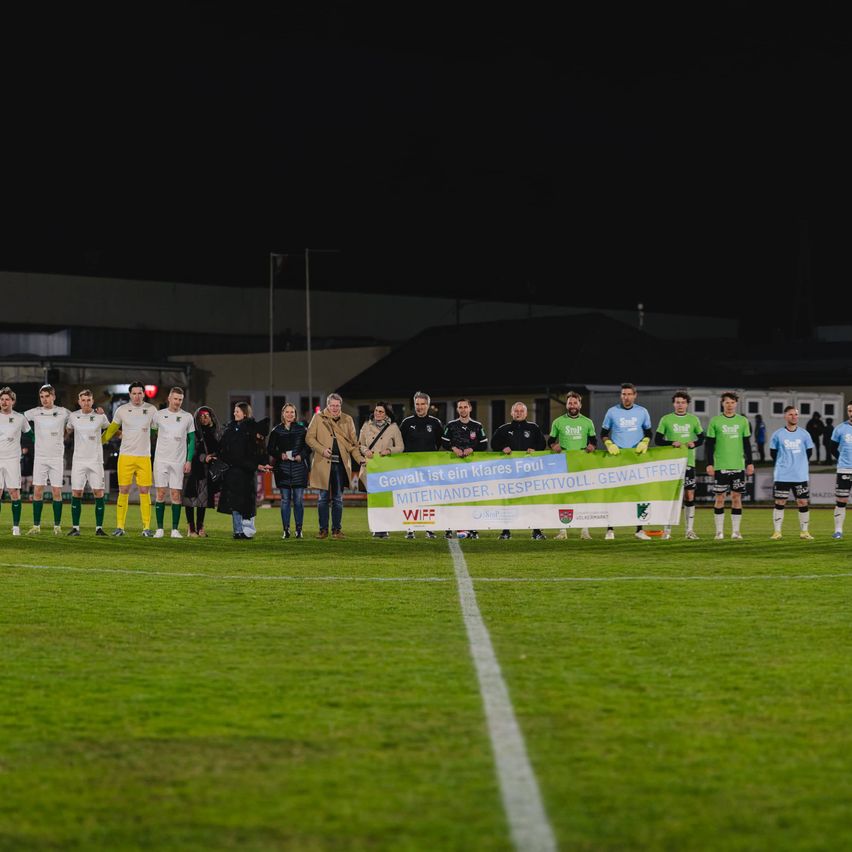 Eine Fußballmannschaft posiert mit einem Banner auf einem Feld bei Nacht. Sie tragen Uniformen und halten gemeinsam das Banner.