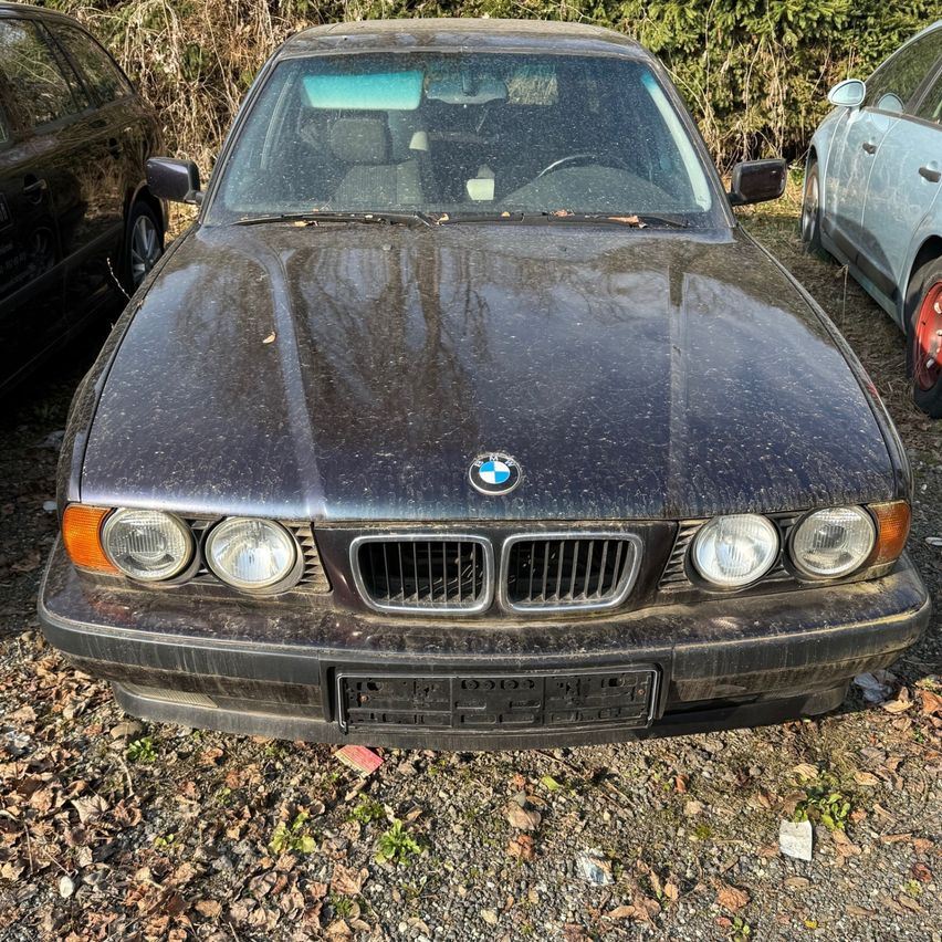 Ein dunkles BMW-Auto mit Schmutz und Ablagerungen, auf einem Schotterplatz geparkt. Es ist von anderen Fahrzeugen umgeben.