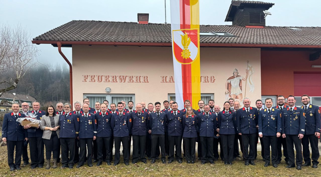 A group of firefighters in uniform are standing in front of a building with a flag and a mural.