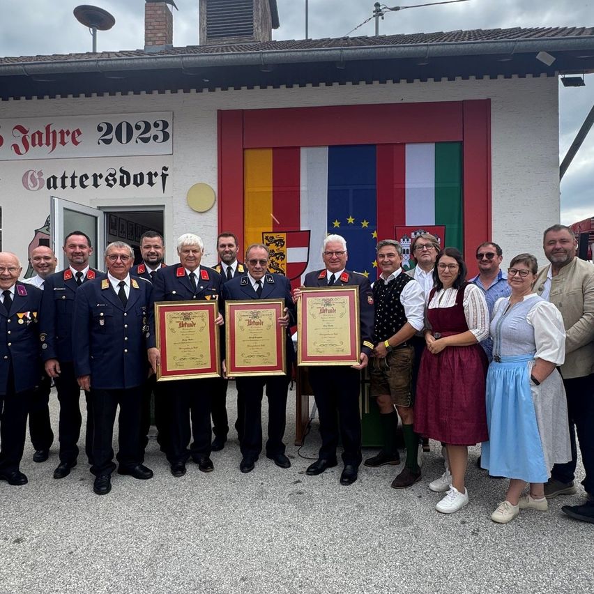 Eine Gruppe von Menschen in Uniformen und traditioneller Kleidung steht vor einem Gebäude mit einer Flagge und einem Schild mit der Aufschrift 'Jahre 2023 Battersdorf'. Sie halten gerahmte Urkunden.