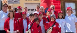 Eine Gruppe von Menschen in roten Jacken und Mützen, einige mit Brillen, stehen vor einem Gebäude. Dahinter befindet sich ein rotes Aufblasobjekt.