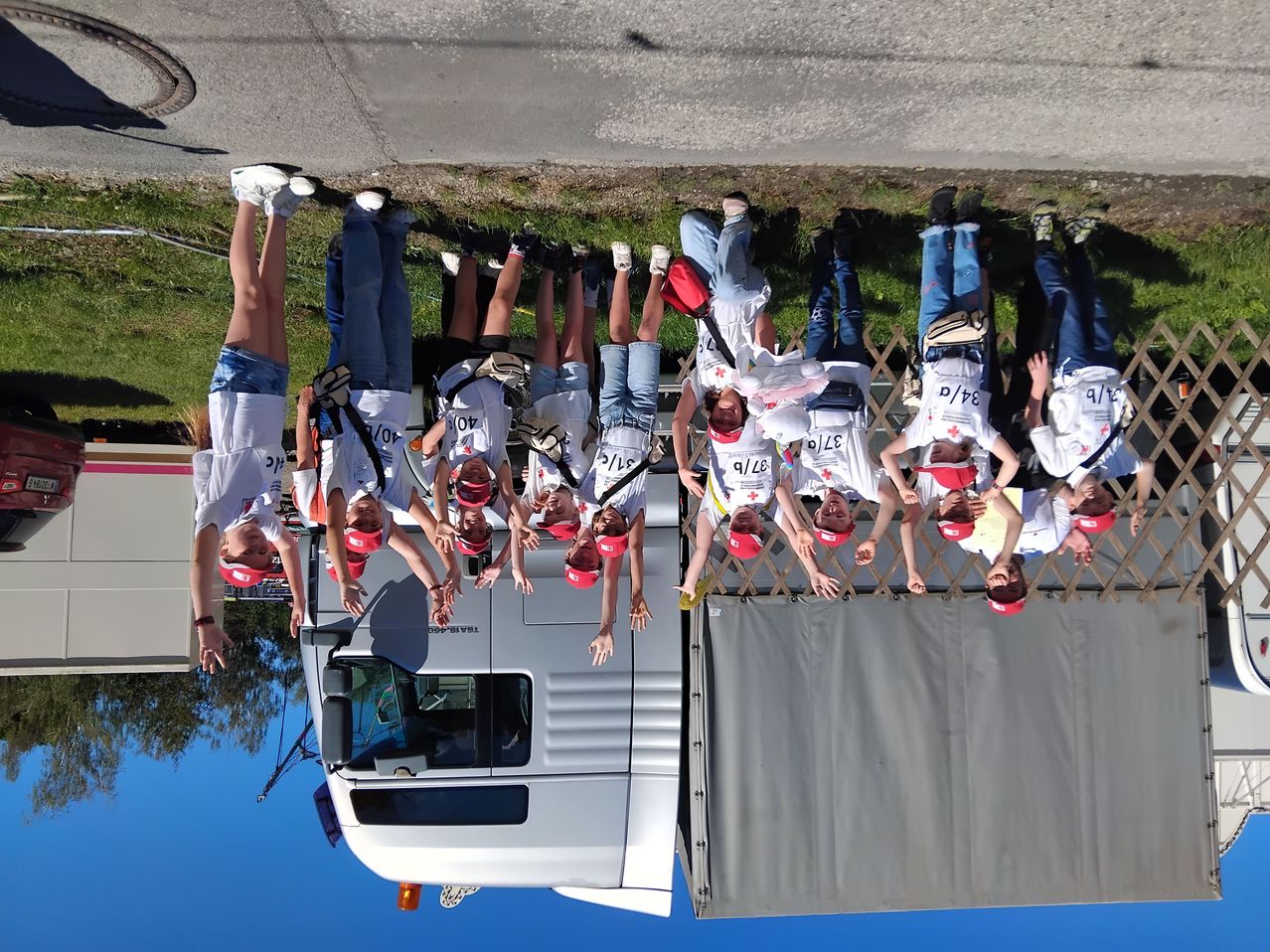 Eine Gruppe von Freiwilligen in weißen T-Shirts und roten Mützen posiert für ein Foto vor einem LKW. Sie stehen in einer Reihe mit erhobenen Händen.