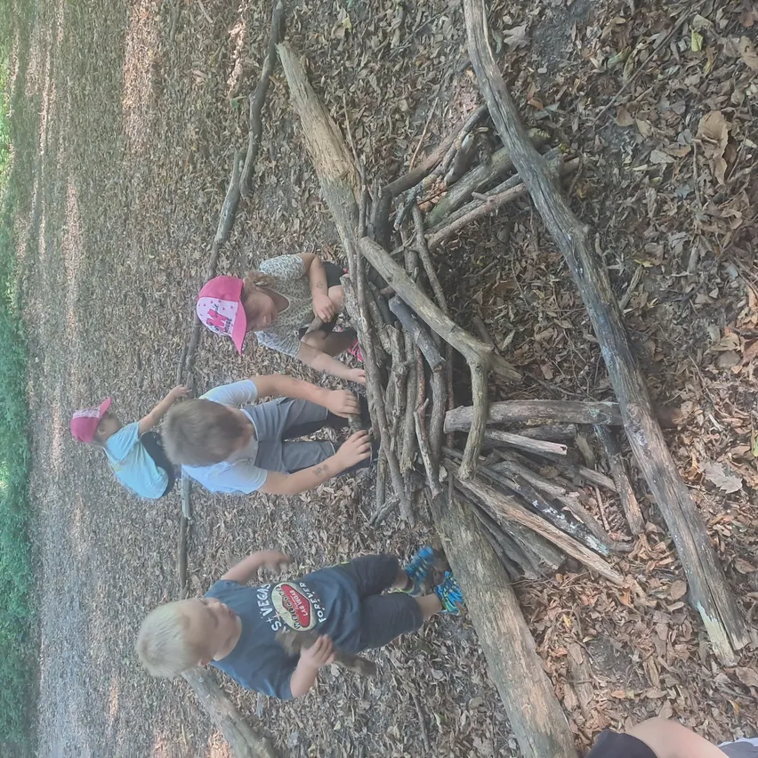 Vier Kinder arbeiten gemeinsam an einem Projekt aus Stöcken im Wald. Ein Kind hockt, während ein anderes steht.
