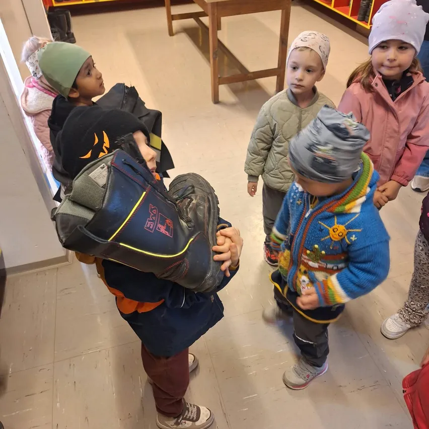Eine Gruppe von Kindern steht in einem Raum mit gefliestem Boden. Ein Kind hält ein Paar Stiefel.