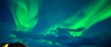 The Aurora Borealis illuminates the night sky with green and blue hues. Stars are visible in the dark sky.