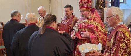 Priester in traditionellen Gewändern führen eine Zeremonie in einer Kirche mit einem Korb Brot durch.