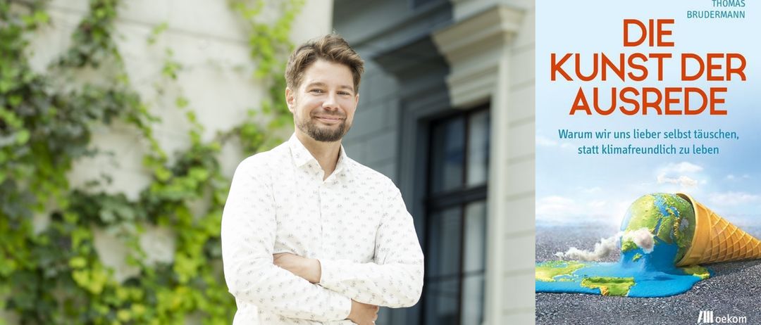 Ein Mann in einem weißen gemusterten Hemd steht lächelnd vor einem Gebäude mit verschränkten Armen.