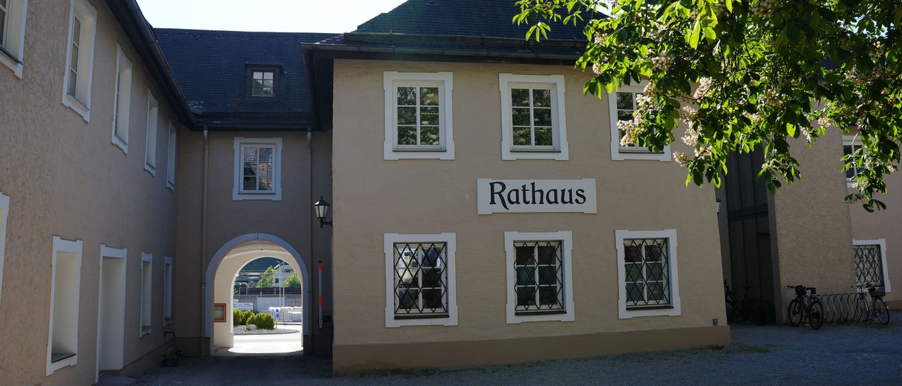 Die Vorderseite eines Rathausgebäudes mit einem grauen Dach und weißen Fensterumrandungen. Über dem Eingang steht das Wort 'Rathaus'.
