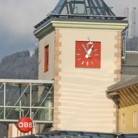 Ein Turm mit einer Uhr unten. Die Uhr hat ein rotes Quadrat und weiße Zeiger.