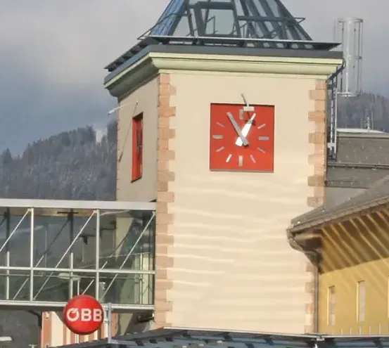 Ein Turm mit einer Uhr unten. Die Uhr hat ein rotes Quadrat und weiße Zeiger.