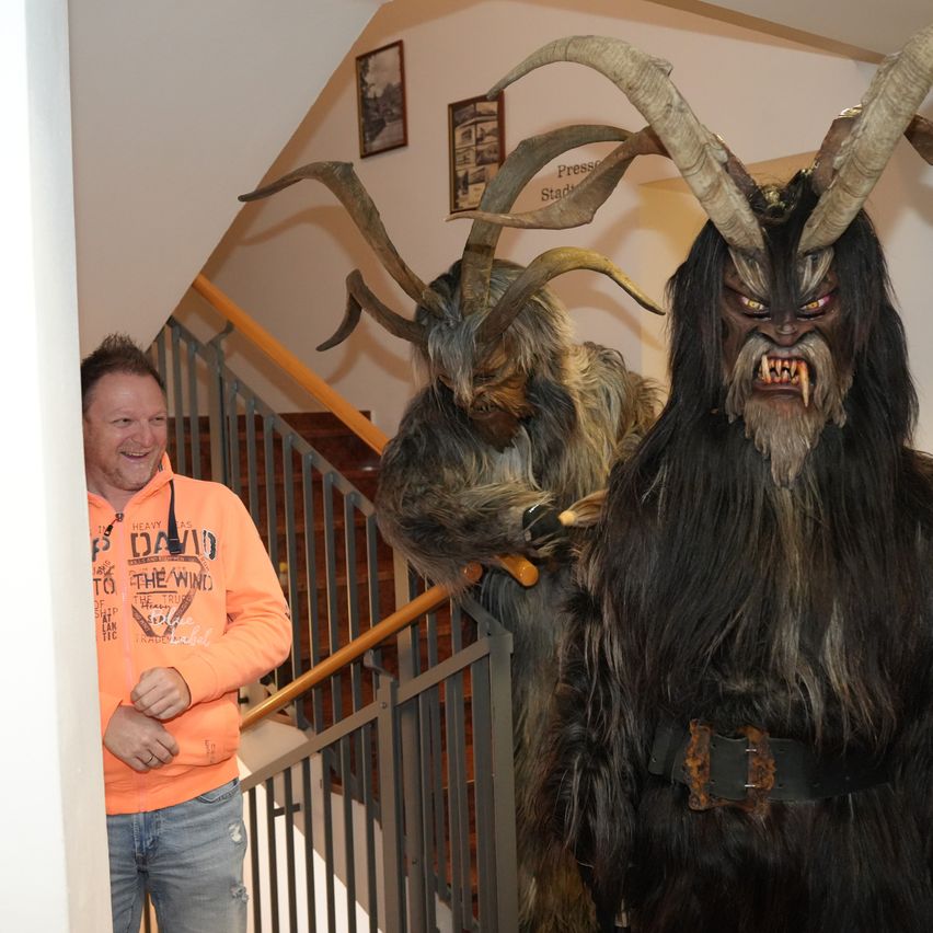 Ein Mann in einem orangefarbenen Hoodie steht neben zwei Personen in Hörnermonsterkostümen auf einer Treppe.