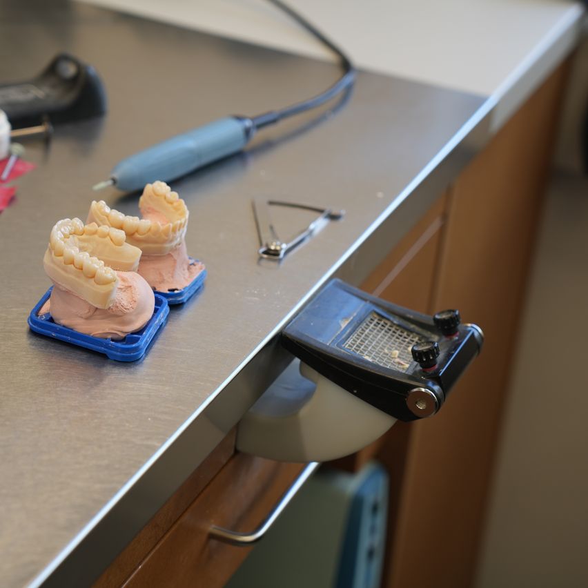 Ein Zahnmodell-Setup mit zwei Zahnsätzen in blauen Schalen, Zahnwerkzeugen und einem Metallgerät auf einem Edelstahltisch.