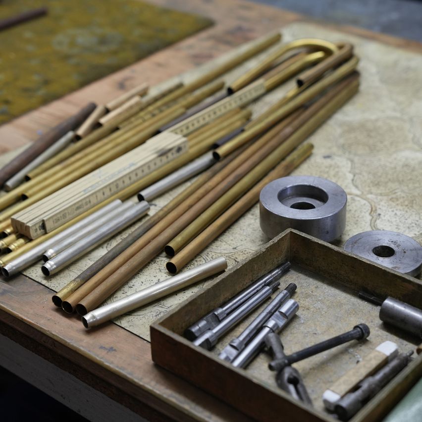 Ein Arbeitstisch zeigt verschiedene Metallrohre, einen Metalllineal und verschiedene Werkzeuge, einschließlich eines Metallrings, Metallstangen und einer kleinen Box mit zusätzlichen Werkzeugen.