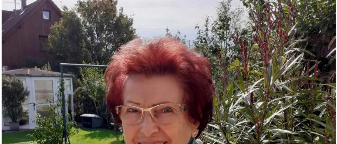 Maria Weiss, eine Frau mit roten Haaren, trägt eine Brille und einen Schal. Sie lächelt, mit einem Haus und Garten im Hintergrund. Der Text lautet 'liest Peter Rossegger' und das Datum und die Uhrzeit sind 'Mi. 29.04.2026 | 19:00 Uhr.'