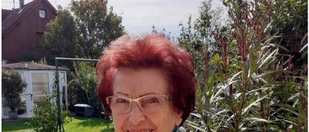 Maria Weiss, eine Frau mit roten Haaren, trägt eine Brille und einen Schal. Sie lächelt, mit einem Haus und Garten im Hintergrund. Der Text lautet 'liest Peter Rossegger' und das Datum und die Uhrzeit sind 'Mi. 29.04.2026 | 19:00 Uhr.'