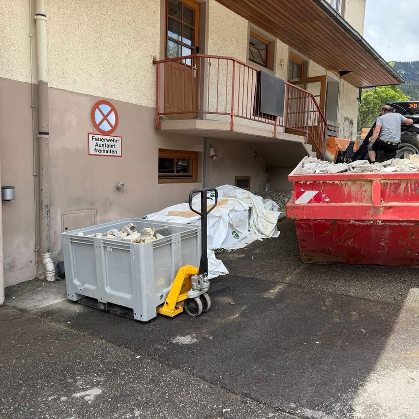 Ein Gebäude mit einem Schild, das Feuerlöscharbeiten verbietet, ein Mann, der einen Traktor bedient, und eine große Mülldeponie mit Schutt gefüllt.