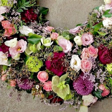 Ein Kranz aus verschiedenen Blumen wie Rosen, Hortensien und anderen Blüten, in einer kreisförmigen Form auf einem grauen Hintergrund angeordnet.