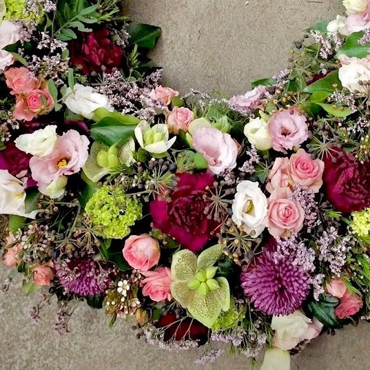 Ein Kranz aus verschiedenen Blumen wie Rosen, Hortensien und anderen Blüten, in einer kreisförmigen Form auf einem grauen Hintergrund angeordnet.