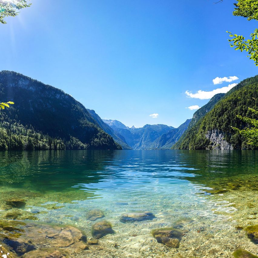 Ein ruhiger Bergsee mit klarem Wasser und felsigem Ufer unter einem blauen Himmel mit Wolken.