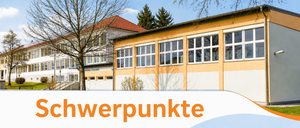 Ein modernes Gebäude mit orangefarbenen Wänden und Glasfenstern, vor dem ein kahler Baum steht. Der Himmel ist klar und blau.