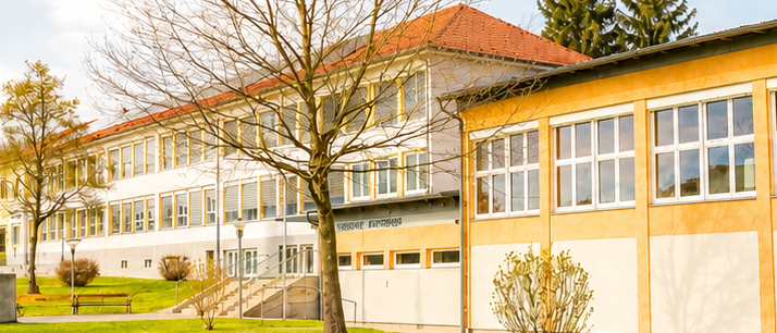 Ein modernes Schulgebäude mit rotem Dach und gelben Akzenten, umgeben von Bäumen und Rasen.