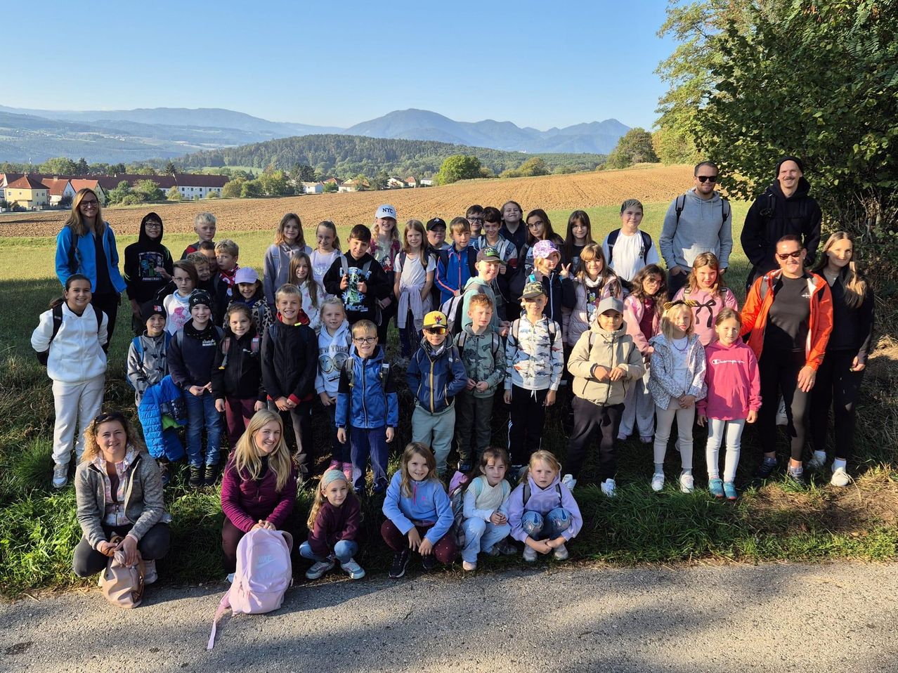 Eine große Gruppe von Kindern und Erwachsenen posiert für ein Foto auf einer Wiese mit Bergen im Hintergrund.