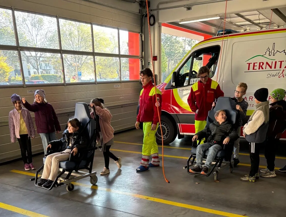 Eine Gruppe von Kindern und Erwachsenen versammelt sich um einen Feuerwehrwagen in einer Garage.