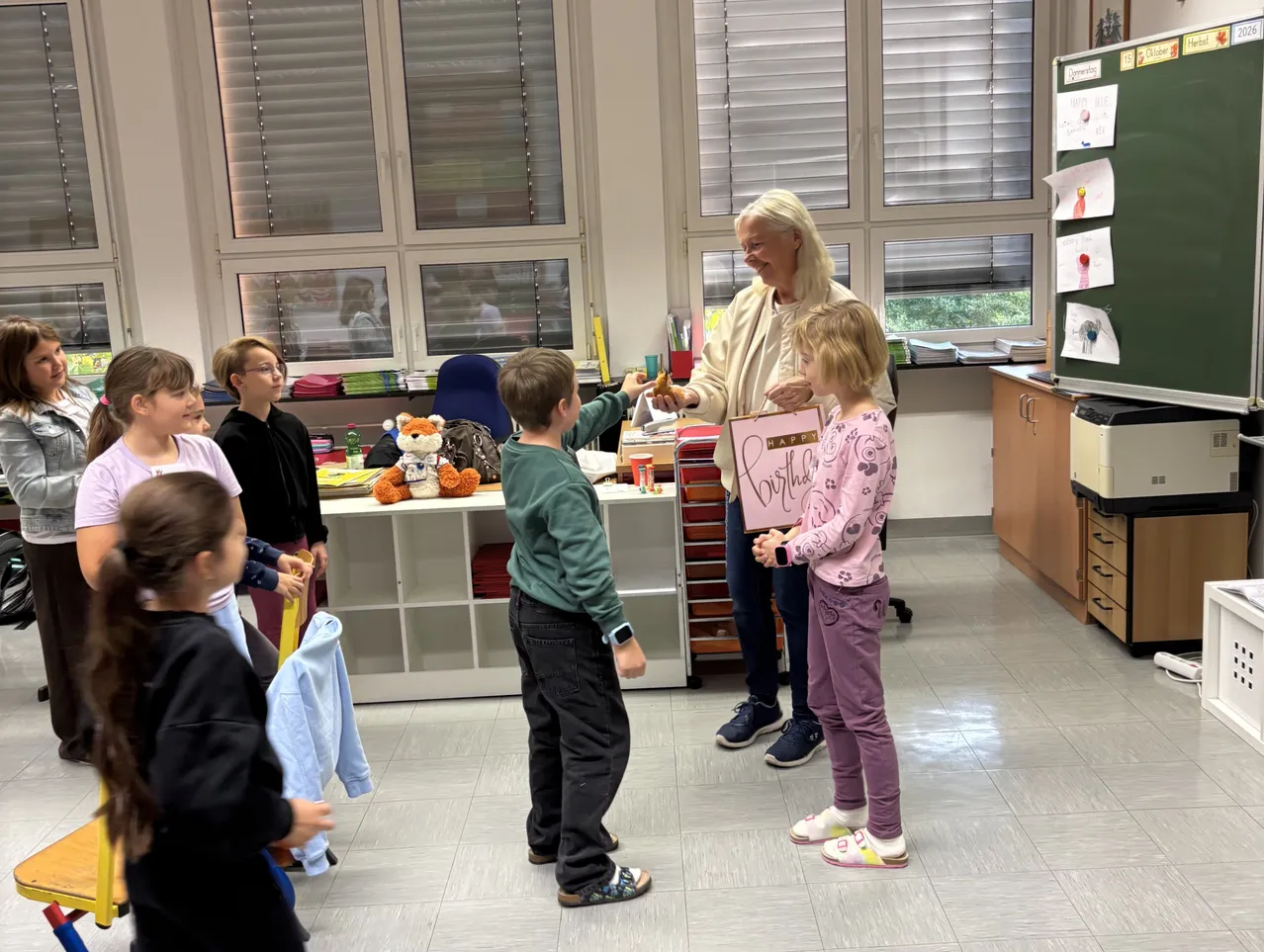 Eine Frau überreicht einem jungen Mädchen einen Geburtstagsgruß in einem Klassenzimmer.