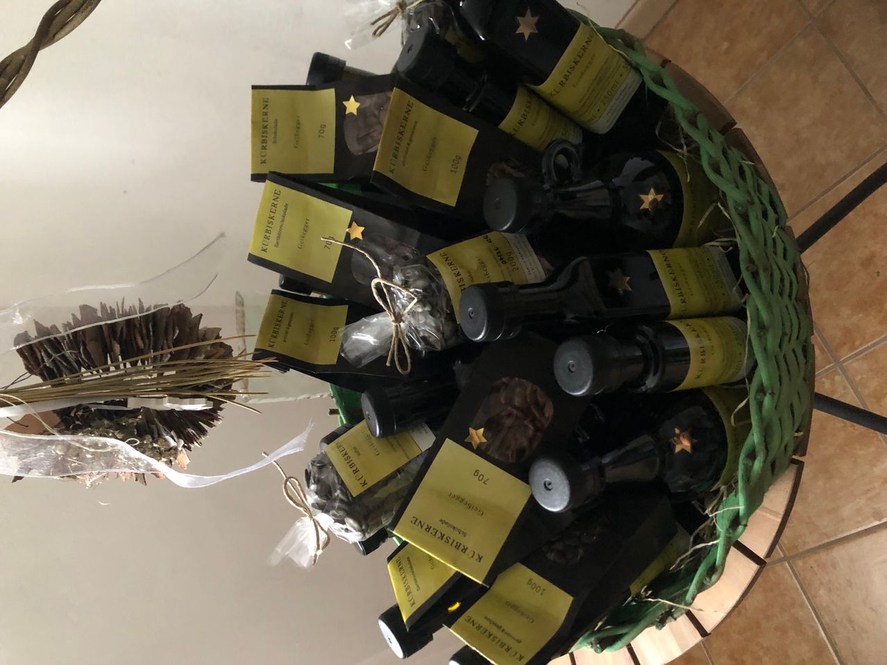 Ein grüner Korb gefüllt mit mehreren Flaschen Wein, jede mit einem gelben Etikett, das einen Stern und den Text 'Kerstbier' zeigt. Die Flaschen sind mit einem Band zusammengebunden. Ein Tannenzapfen ist neben dem Korb platziert.