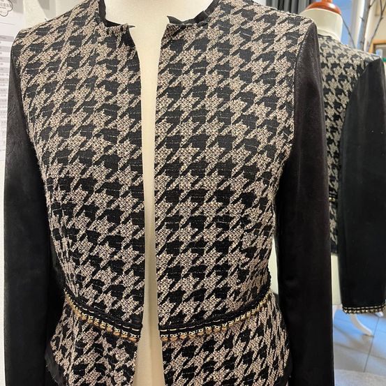 Ein Dummy zeigt eine schwarz-weiße Jacke mit Jagdhund-Karomuster und einer perlenbesetzten Taille auf weißem Hintergrund.