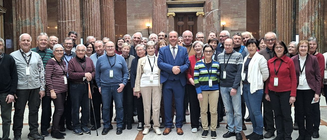 Eine Gruppe von Menschen mit Namensschildern posiert für ein Foto in einem großen Saal mit Marmorsäulen und historischen Gemälden an den Wänden.