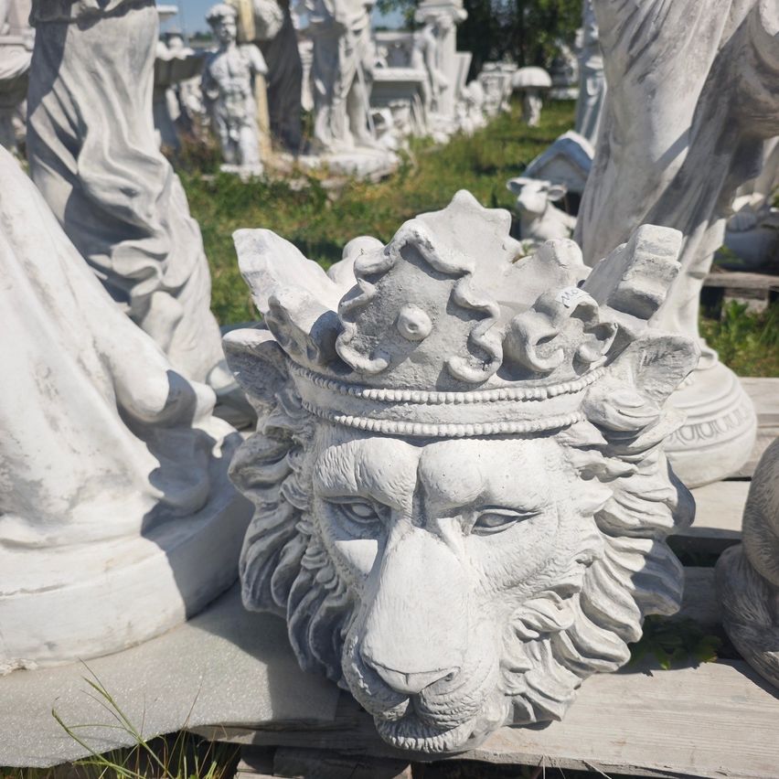 Nahaufnahme einer Löwenstatue mit Krone, umgeben von anderen Statuen und Grün.