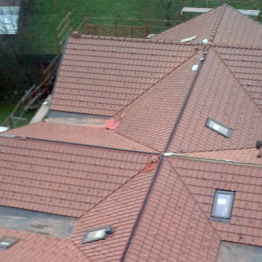 Ein Blick von oben auf ein Haus mit einem roten Ziegeldach. Es gibt mehrere Fenster auf dem Dach und auf der linken Seite befindet sich ein Gerüst.