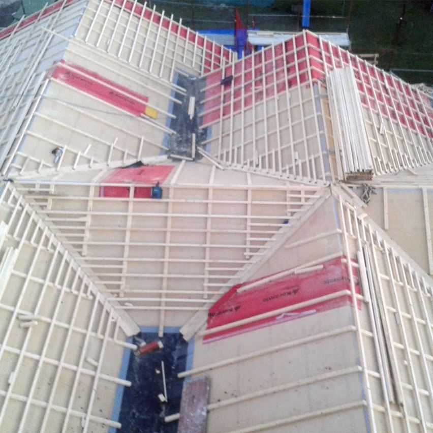 Eine Vogelperspektive auf das Dach eines Gebäudes im Bau. Das Dach besteht aus einer Kombination aus roten und weißen karierten Mustern mit einem weißen Holzrahmen.